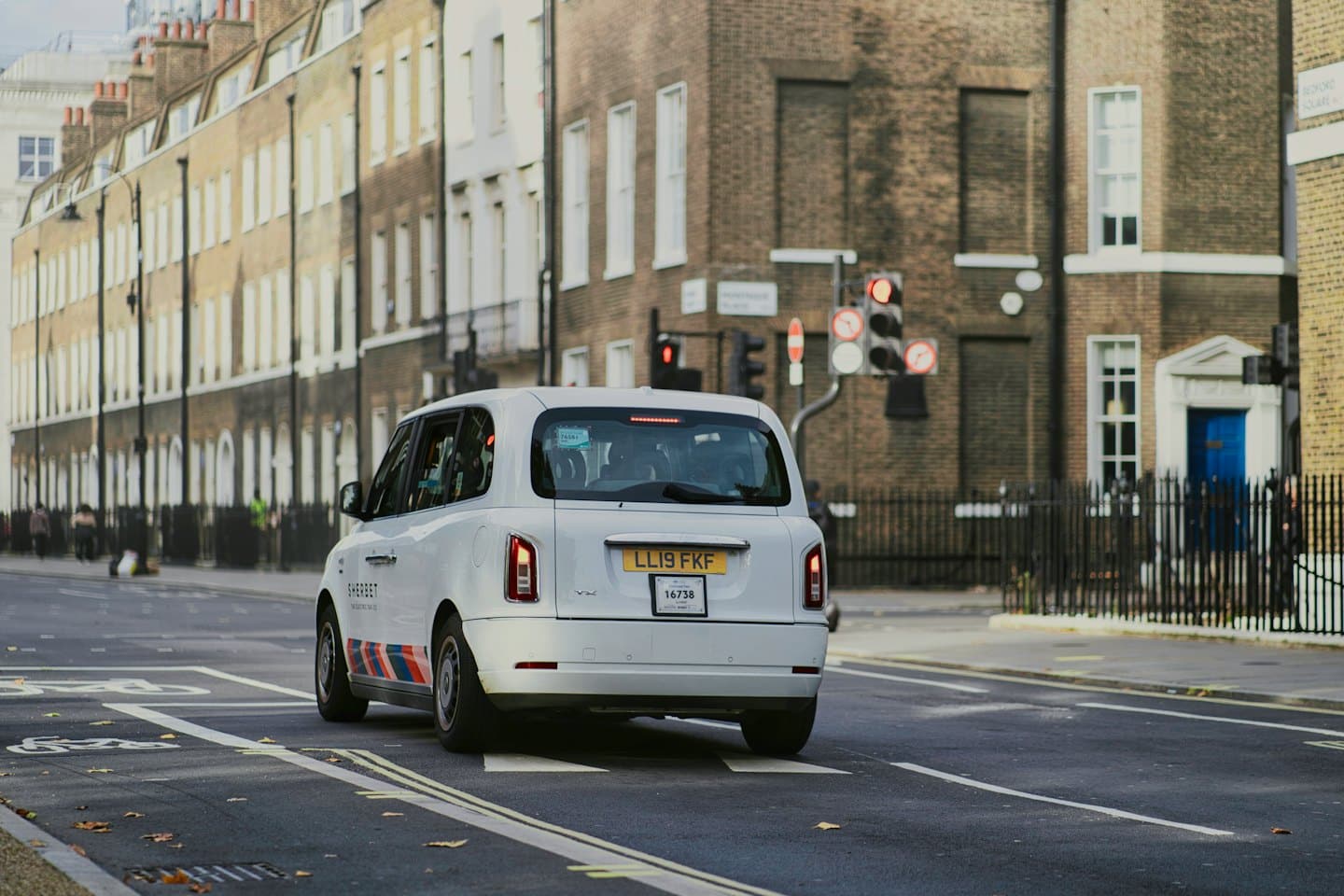 Moderner weißer Taxi fährt auf einer Stadtstraße davon.