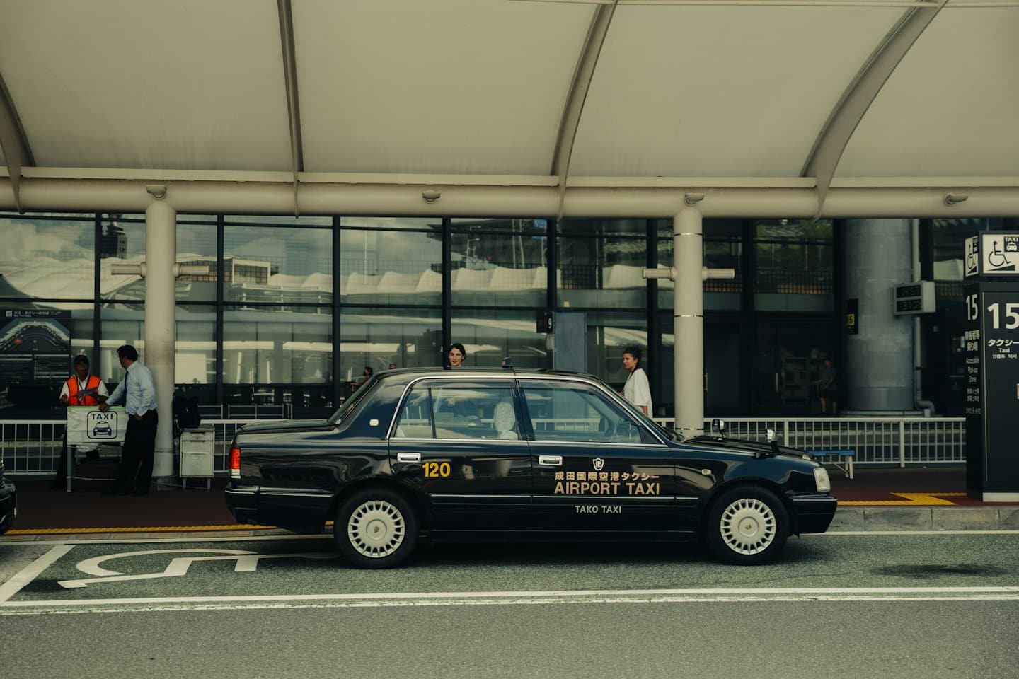 Schwarzes Taxi am Flughafenterminal mit Menschen am Taxistand.